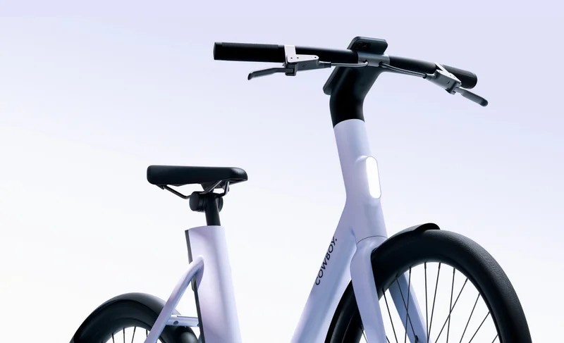 A Cowboy bike with a smartphone mounted on the handlebars, displaying navigation directions and speed on the app interface. A large white number “5” is visible in the background.