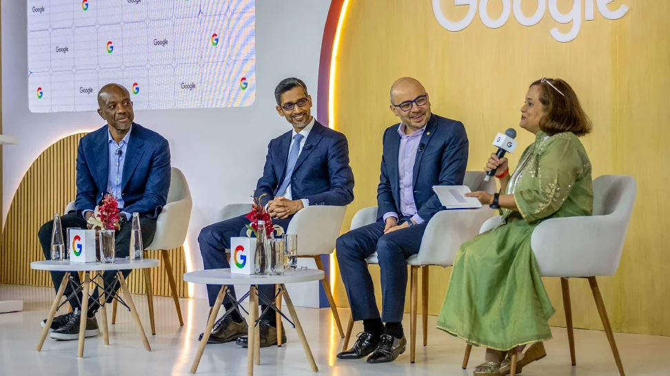 Woman on a panel on stage speaking into microphone with Google logo in background.