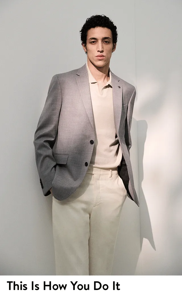 A man wearing a grey suit jacket with a polo sweater and pants.